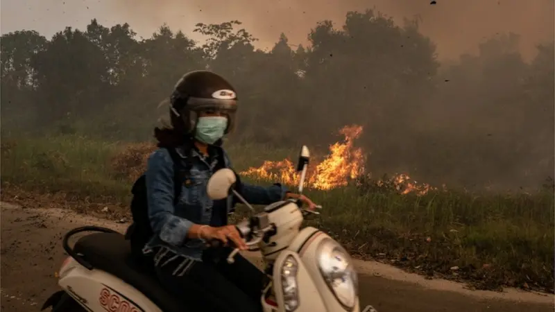 Warga melintasi sebuah lahan yang tengah terbakar. (Getty Images)